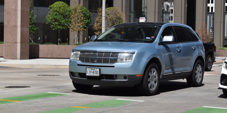 A sky-blue Lincoln MKX luxury SUV, cruising in the downtown financial district – Ford, cheap car insurance. 
