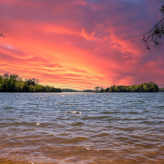 A gorgeous spring landscape at Lanier Point Park with rippling blue water surrounded by lush green trees and plants with powerful cloud at sunset at Lake Lanier in Gainesville – cheap car insurance in Georgia.