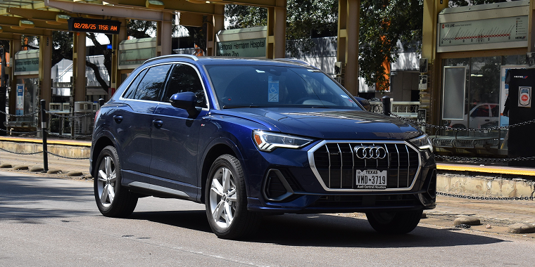 A portrait of a luxurious blue Audi Q5 SUV cruising in the medical district of downtown Houston, Texas. In the background, there is a metro station and the UT Health Science Center — Audi, cheap car insurance.