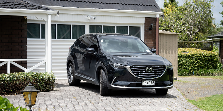 Front right view of black Mazda CX-9 Generation II (2016) in front of white tilt-up retractable garage door in Auckland, New Zealand - November 22, 2022 – Mazda, cheap car insurance.