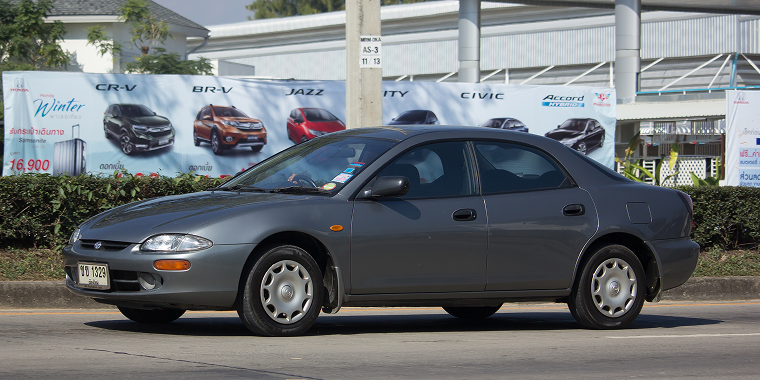 Chiang Mai, Thailand – January 8, 2018: A Mazda Protege driving on a street in front of a car dealership. Cheap car insurance. 