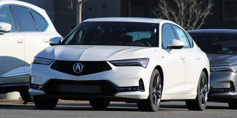 A white next-generation Acura Integra driving down a street past cars in Detroit, Michigan. — Cheap car insurance.