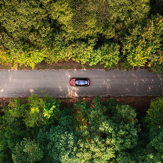 A red car drives along a narrow road surrounded by dense green forest in Evansville, Missouri, captured from an overhead view.