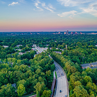 Aerial view of a road winding through dense green forests and residential neighborhoods in Georgia at sunset.