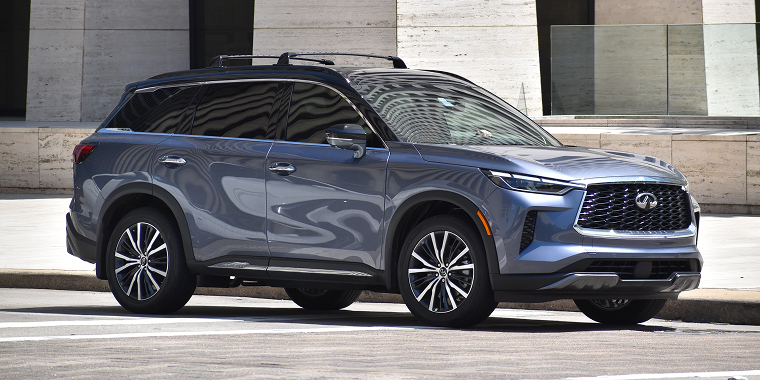 A portrait of a blue metallic colored Infiniti QX60 SUV cruising in a downtown financial district. Cheap car insurance.