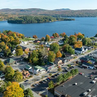 Aerial view of Schroon Lake, NY, showcasing the town's buildings, colorful autumn trees, and lakeside setting with a peaceful small-town atmosphere.