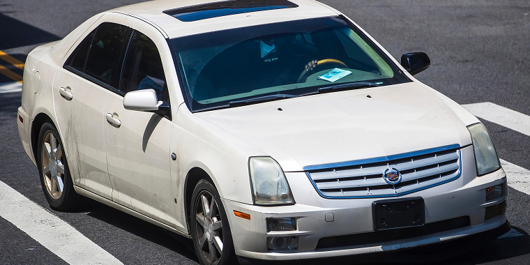 A white Cadillac STS Seville Touring Sedan driving down the street on a sunny day — Cheap car insurance. 
