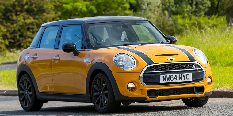 Stony Stratford, UK - June 4th 2023: 2014 orange MINI Cooper S classic car travelling on an English country road – MINI Cooper, cheap car insurance.