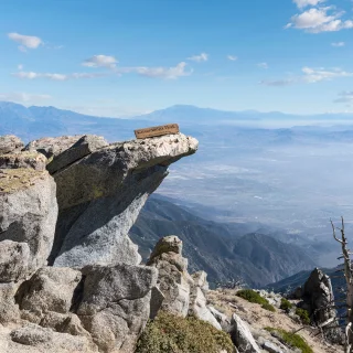 Rocky mountain viewpoint at Cucamonga Peak in California, overlooking the San Gabriel Valley under a blue sky with scattered clouds.