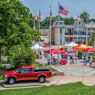 Kenner, Louisiana outdoor farmers market with vendor tents, shoppers, and American flags in a town square