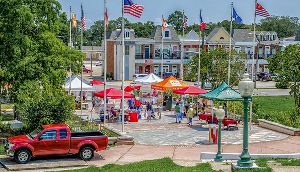 Kenner, Louisiana outdoor farmers market with vendor tents, shoppers, and American flags in a town square