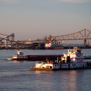 Port Allen, Louisiana Mississippi River industrial waterfront with tugboats, barge traffic, and bridge at sunset