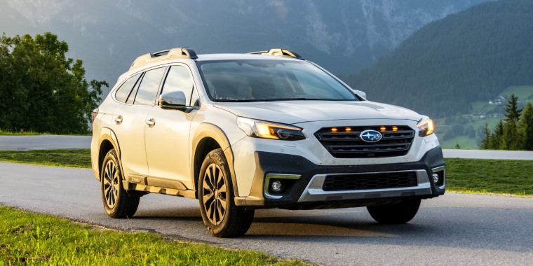 White family SUV Subaru Outback in the evening at sunset on the road in the mountains. Off-road car in the Alps in nature between the mountains. Cheap car insurance for Subaru.