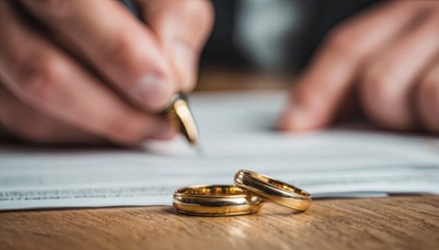 Person signing divorce documents with wedding rings on the table, representing marital status and auto insurance rates.