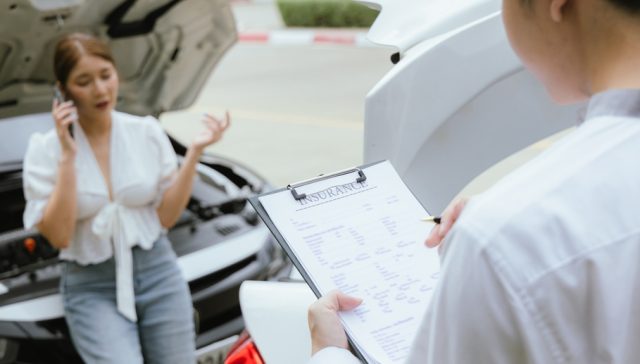 Driver on phone beside a damaged car speaking with an insurance agent about liability after hitting an uninsured motorist