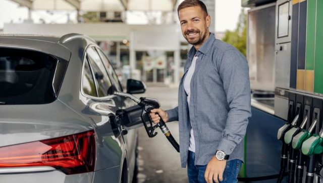Man fueling his car at a gas station while looking for ways to save gas mileage.