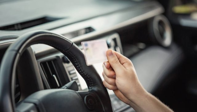 Driver holding a suspended driver's license inside a vehicle, highlighting situations where you may need an SR-22 after a license suspension.