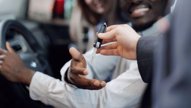 A rental agent hands over car keys to a driver inside a vehicle, illustrating the process for a foreign rent car in the US.