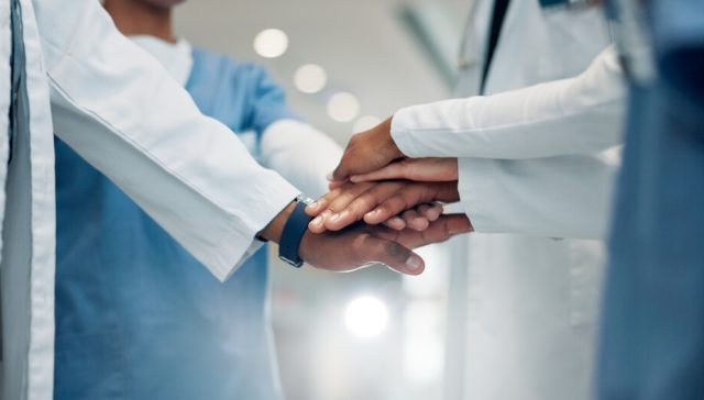 Healthcare professionals in medical uniforms place their hands together in a gesture of teamwork, symbolizing coordinated care supported by medicaid insurance.
