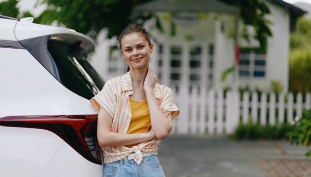 Young woman standing beside a parked SUV in a residential neighborhood, where ZIP codes can affect car insurance costs.