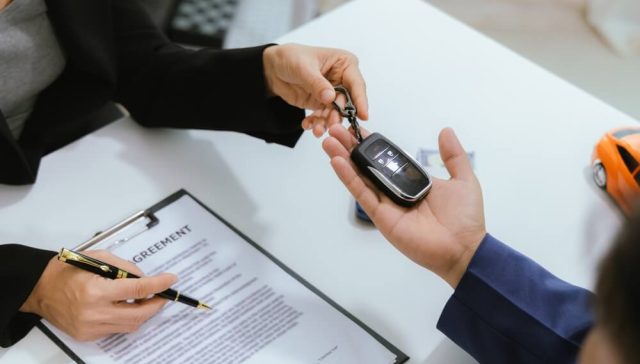 Car buyer receiving vehicle keys while reviewing requirements when you finance your car.