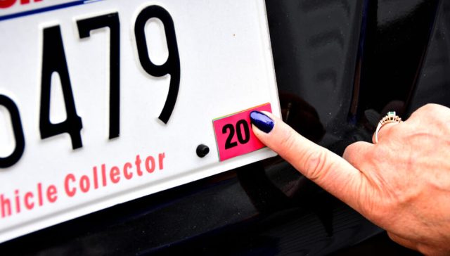 Hand pointing to a registration sticker on a car license plate, a key step when registering your car in a new state.