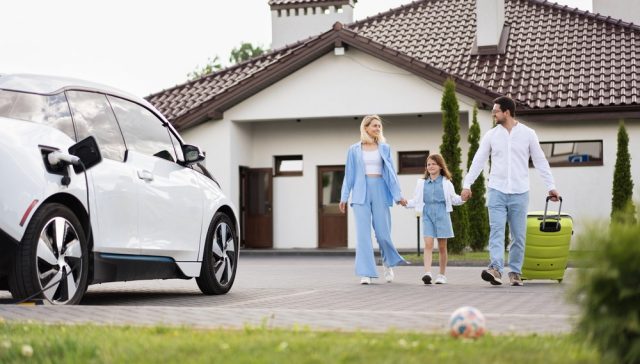 Family walking together outside their home beside a white electric car, illustrating home and auto insurance bundling.