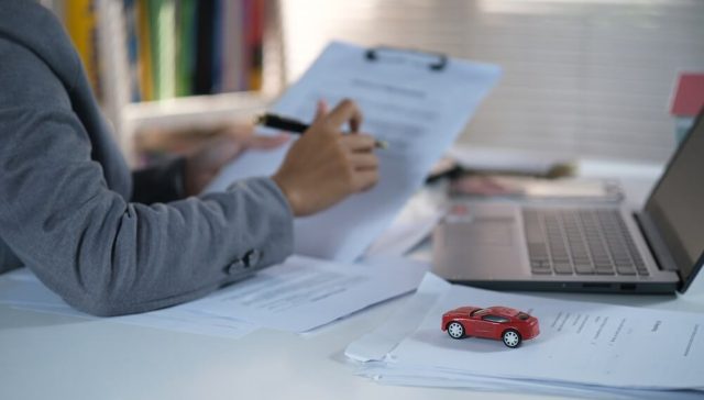 Insurance professional reviewing paperwork beside a laptop and a miniature red car, illustrating the documentation involved in an SR-22 insurance filing.