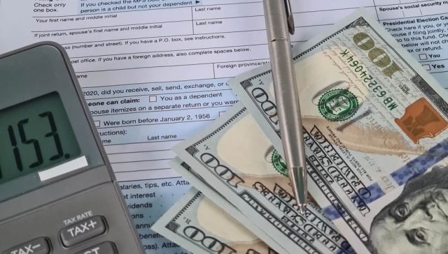 Close-up of a 1040 u.s. tax return with a calculator, pen, and hundred-dollar bills, suggesting budgeting ideas like tax refund auto insurance.