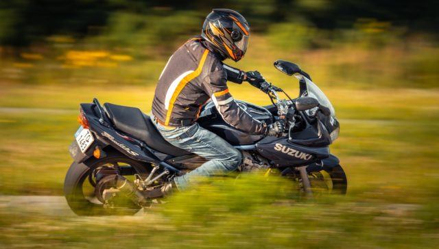 Rider wearing a helmet while driving a motorcycle on the road, showing why motorcycle insurance is mandatory.