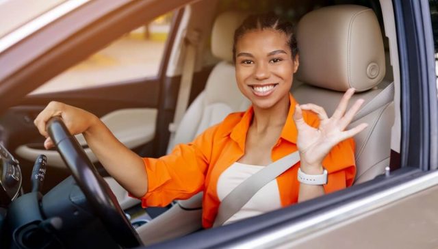 Smiling woman driving a car and gesturing OK, representing confidence after choosing affordable car insurance options.