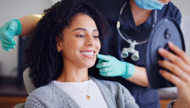 Woman smiling at her teeth during a dental visit, showing care covered by dental insurance included in health insurance.