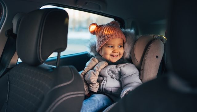 Small child bundled up for winter in a car seat in the back seat of a car.