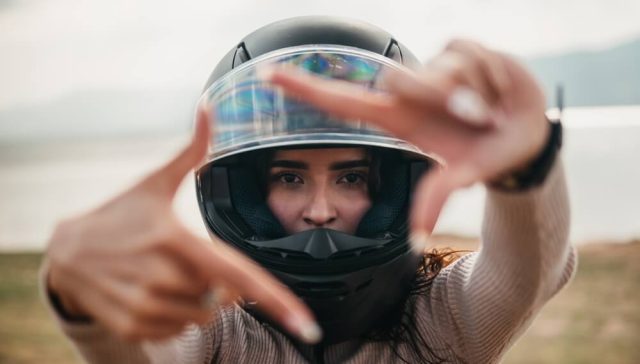 Woman wearing a full-face motorcycle helmet frames the camera with her hands, highlighting Motorcycle Helmets and Insurance.
