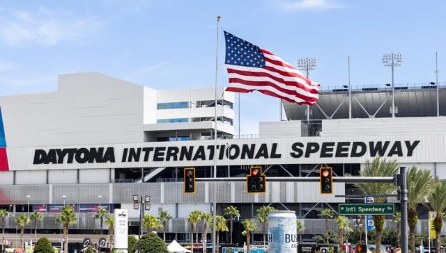 Daytona International Speedway entrance with an American flag flying above the iconic racing venue.