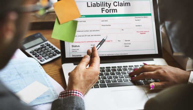 Two people reviewing a small business liability claim form on a laptop with a calculator and paperwork nearby.