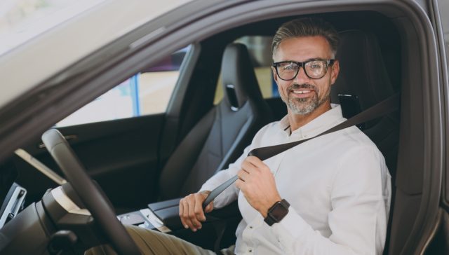 Driver fastening his seat belt in a car while preparing documents for a car insurance binder.