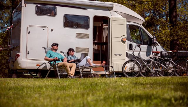 Couple relaxing beside their motorhome while considering how to compare RV insurance.