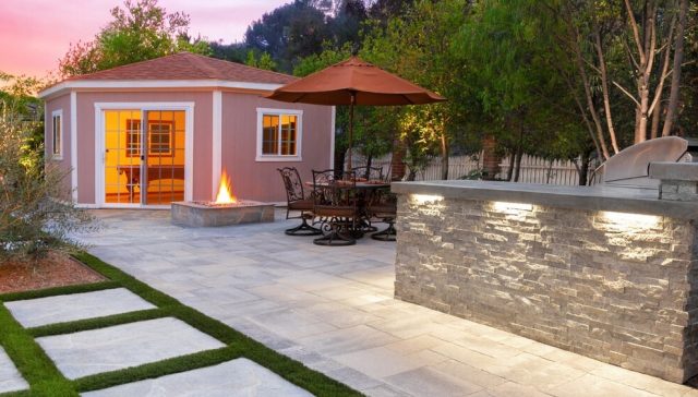 Backyard patio with a detached studio, fire pit, dining area, and outdoor kitchen, showing how homeowners coverage protects your backyard investments.