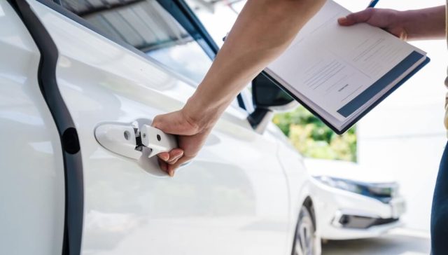 Person holding documents while opening a white car door, illustrating changes to an auto insurance policy through an endorsement.