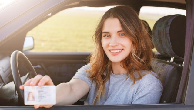 Young driver holding a driver’s license while sitting behind the wheel of a car.