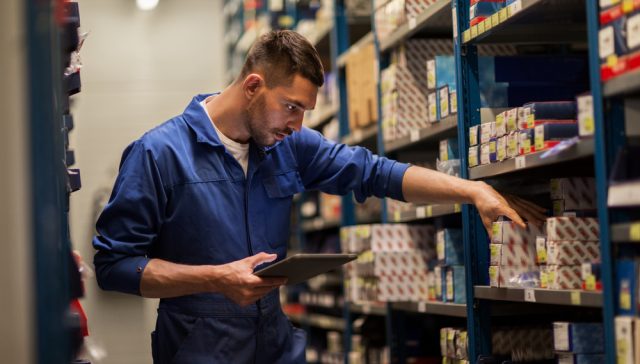 Auto parts store employee checking OEM car parts inventory on shelves.